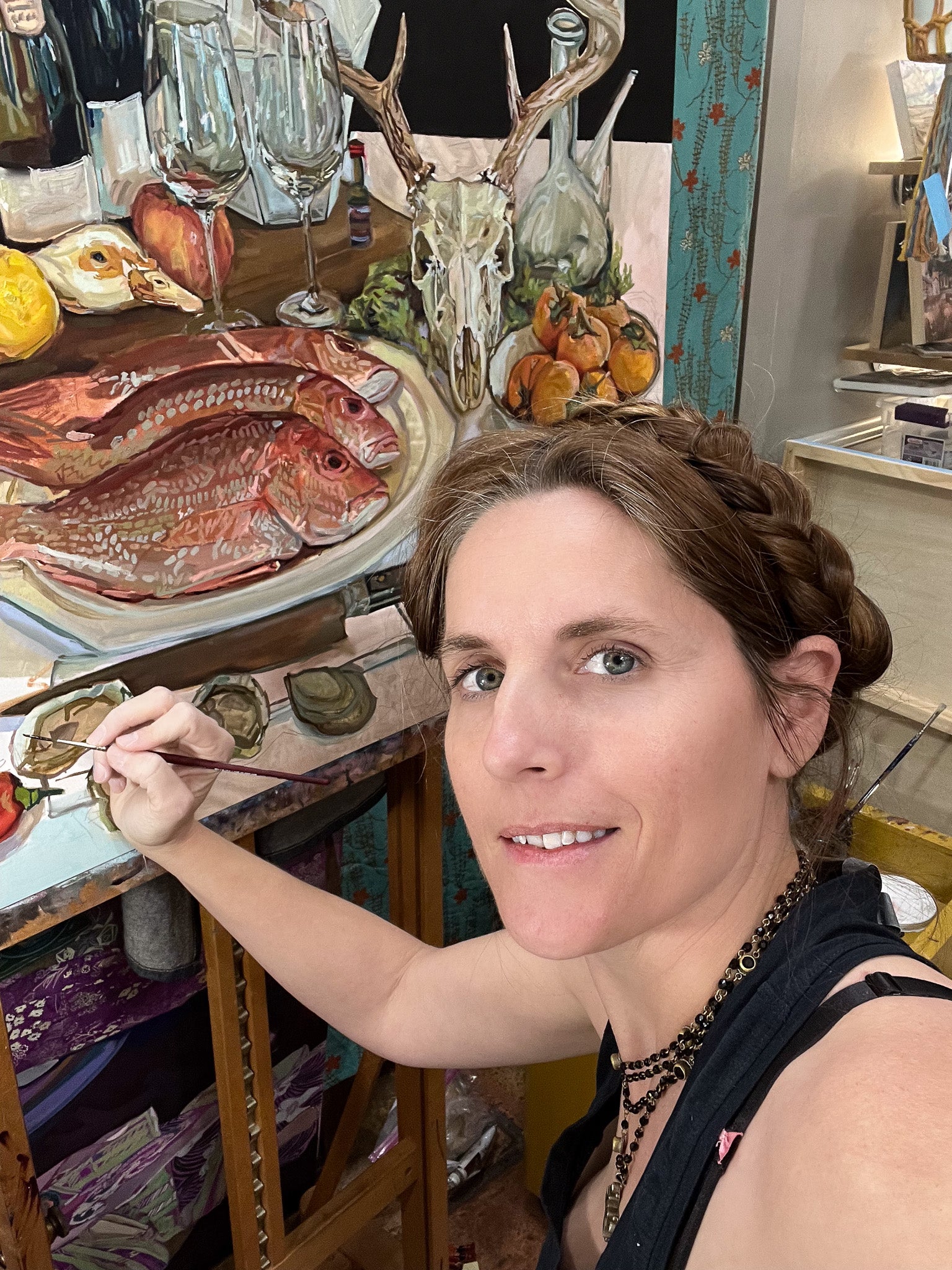Artist Courtney Leigh Holder painting food still life oil painting at studio in Texas with deer skull and fish painting in background.