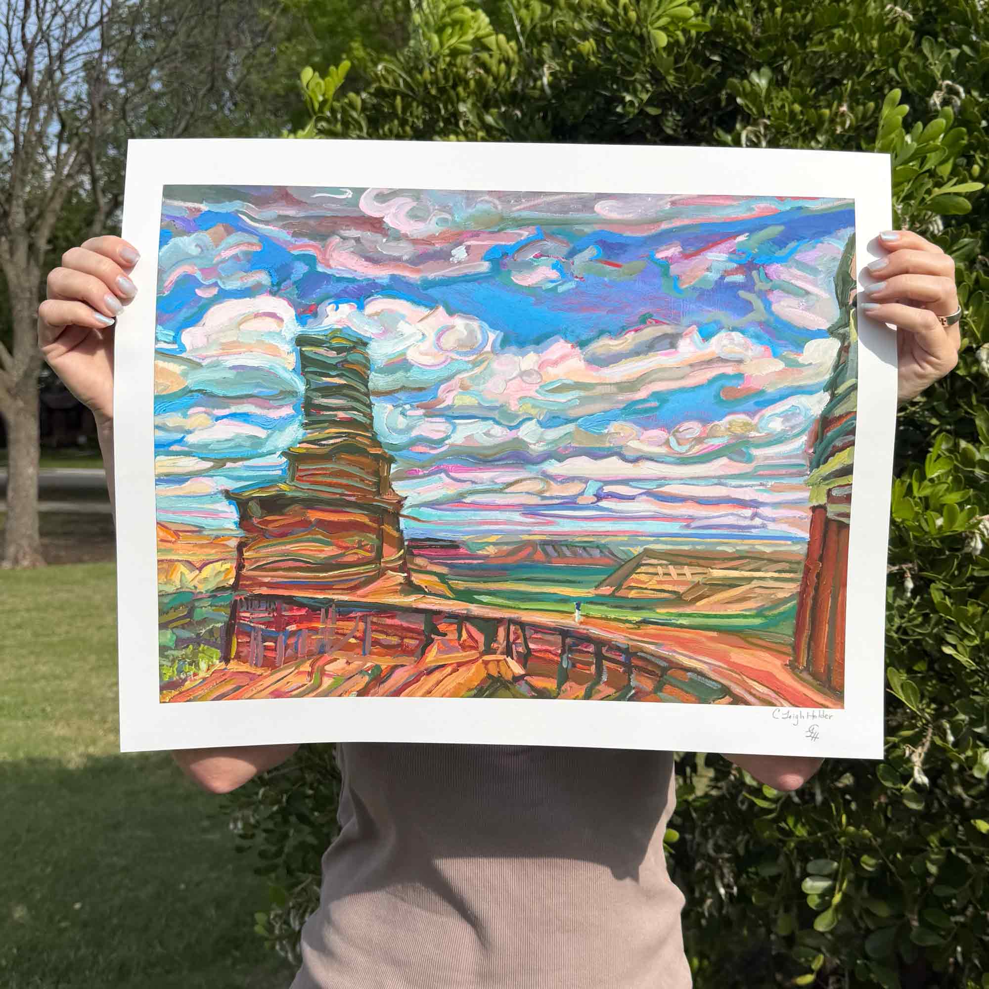 Artist holding a colorful landscape print of canyon painting outdoors
